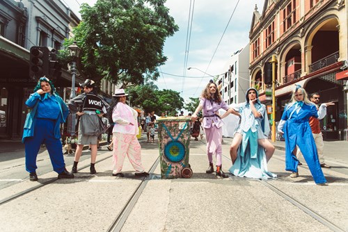 Six fashionable dressed people in Gertrude Street, with a plastic bin in which a speaker has been mounted