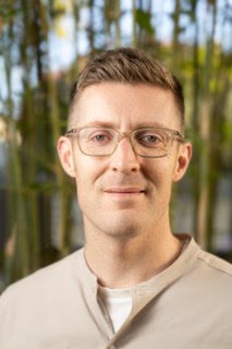 Headshot of Luke wearing brown glasses and brown shirt
