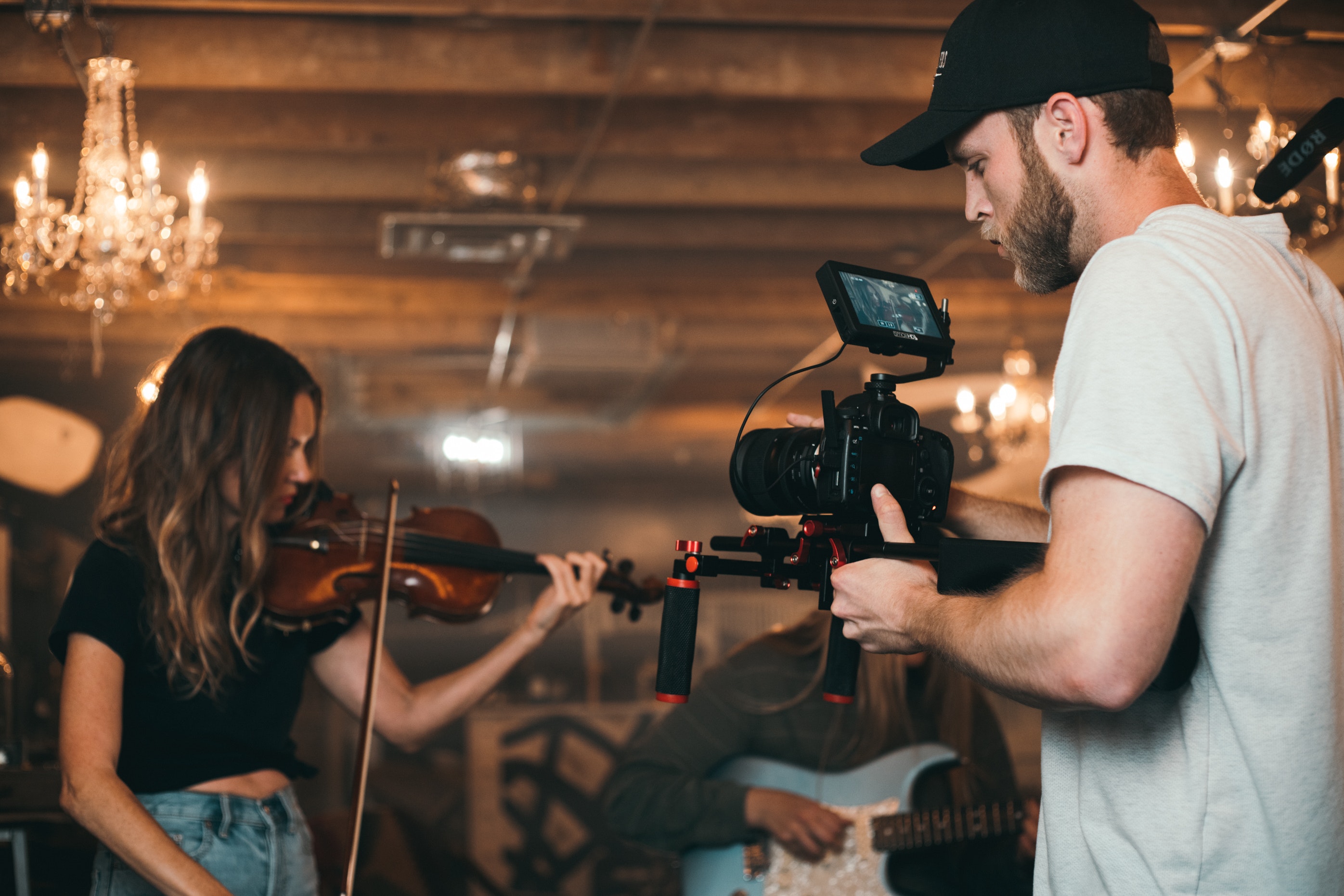 Musicians being photographed while performing in a large room with a chandelier behind them