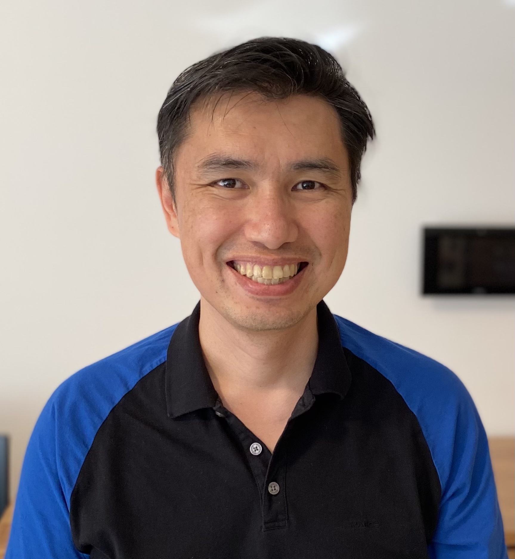 A person with short hair wearing a blue and black shirt smiling.