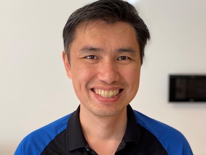 A person with short hair wearing a blue and black shirt smiling.