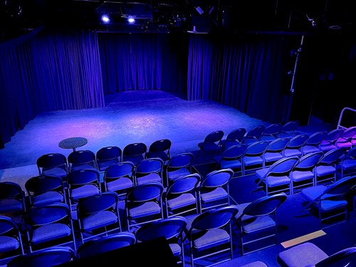 A row of chairs facing a stage. The lighting is purple.