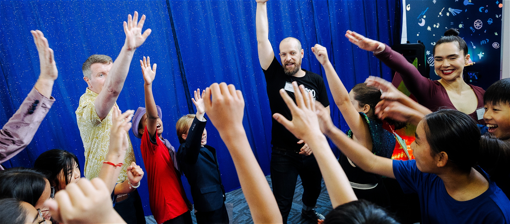 Three facilitators and a dozen children smiling and raising their arms enjoying a writing workshop