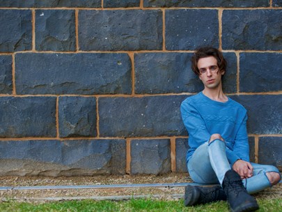 A teenage boy dressed in blue, leaning against a brick wall.