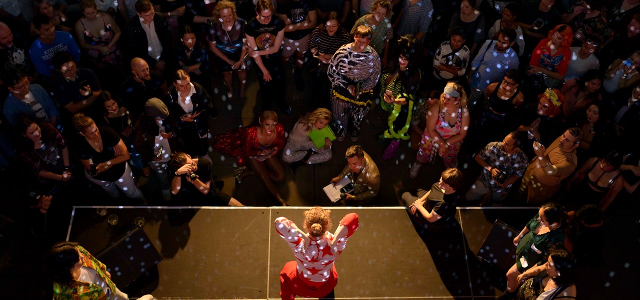 Performer on stage with arms raised and audience all around them