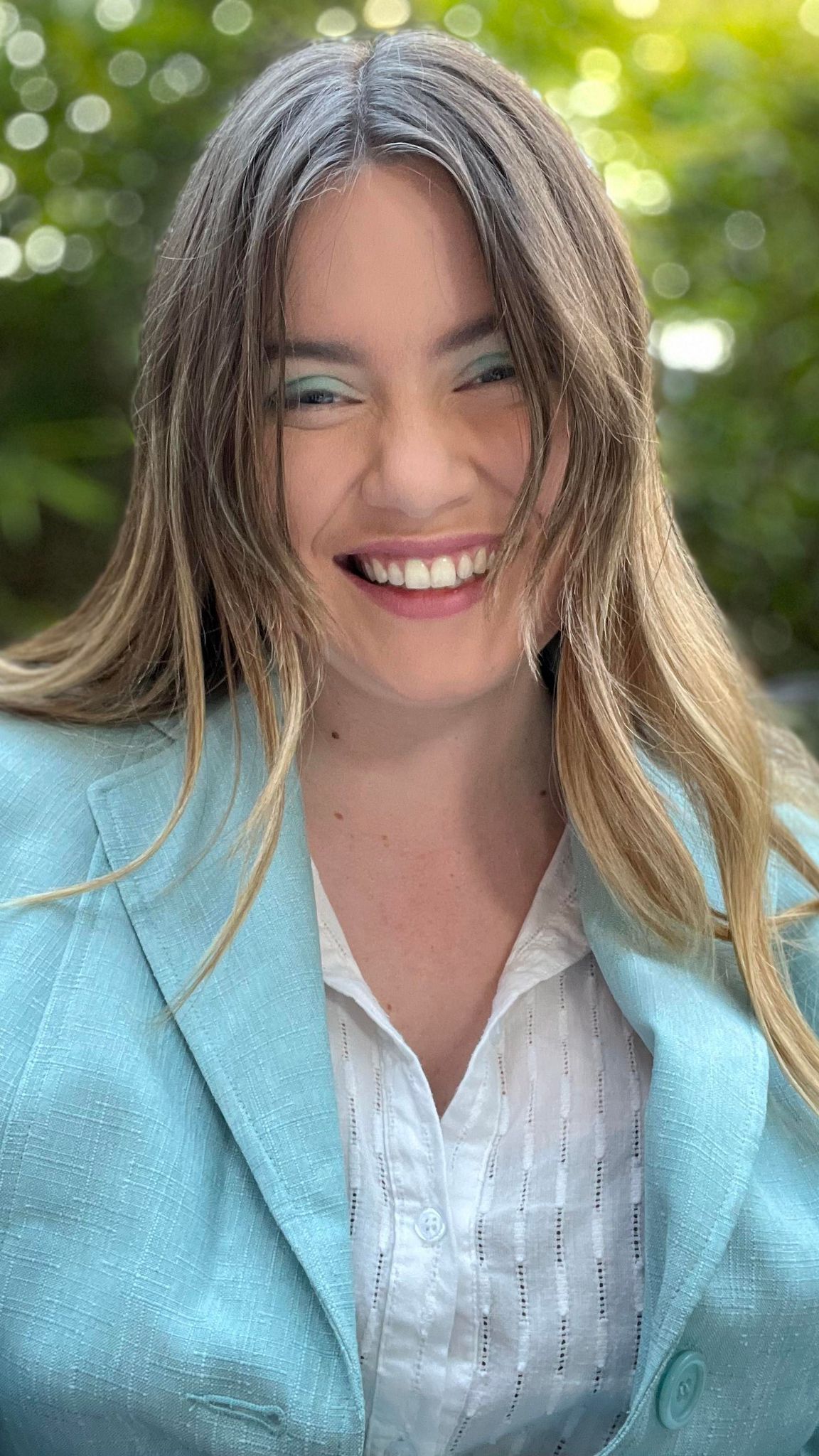 A smiling headshot of Ellis, she has blonde hair and a blue blazer that matches her blue eyeshadow.