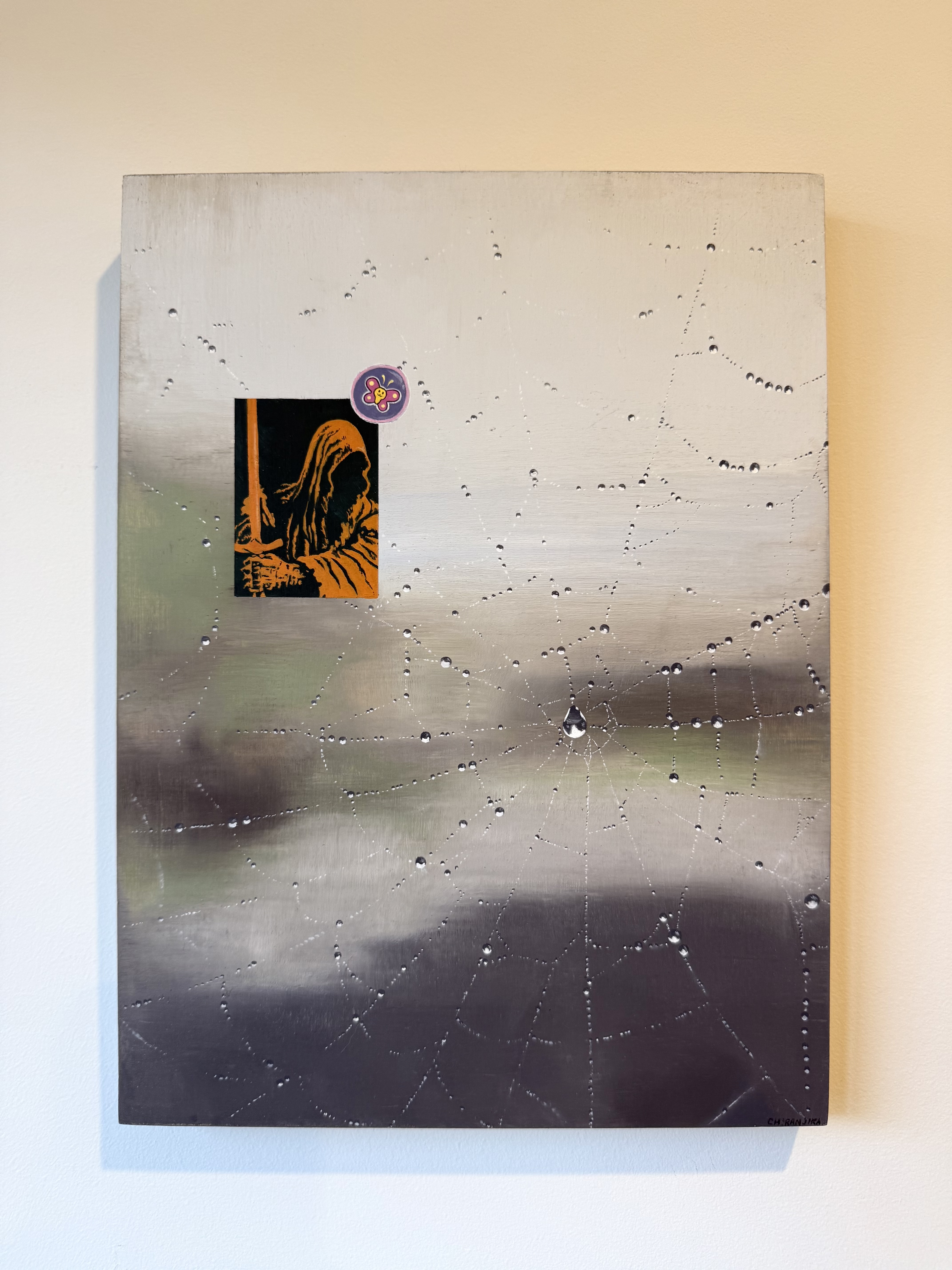 A photo of a painting. The main feature is a spiders web. There is a small etching and a butterfly-like emblem.