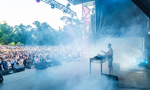 A DJ on a large stage before a large crowd at Midsumma Carnival 2019; lots of smoke present