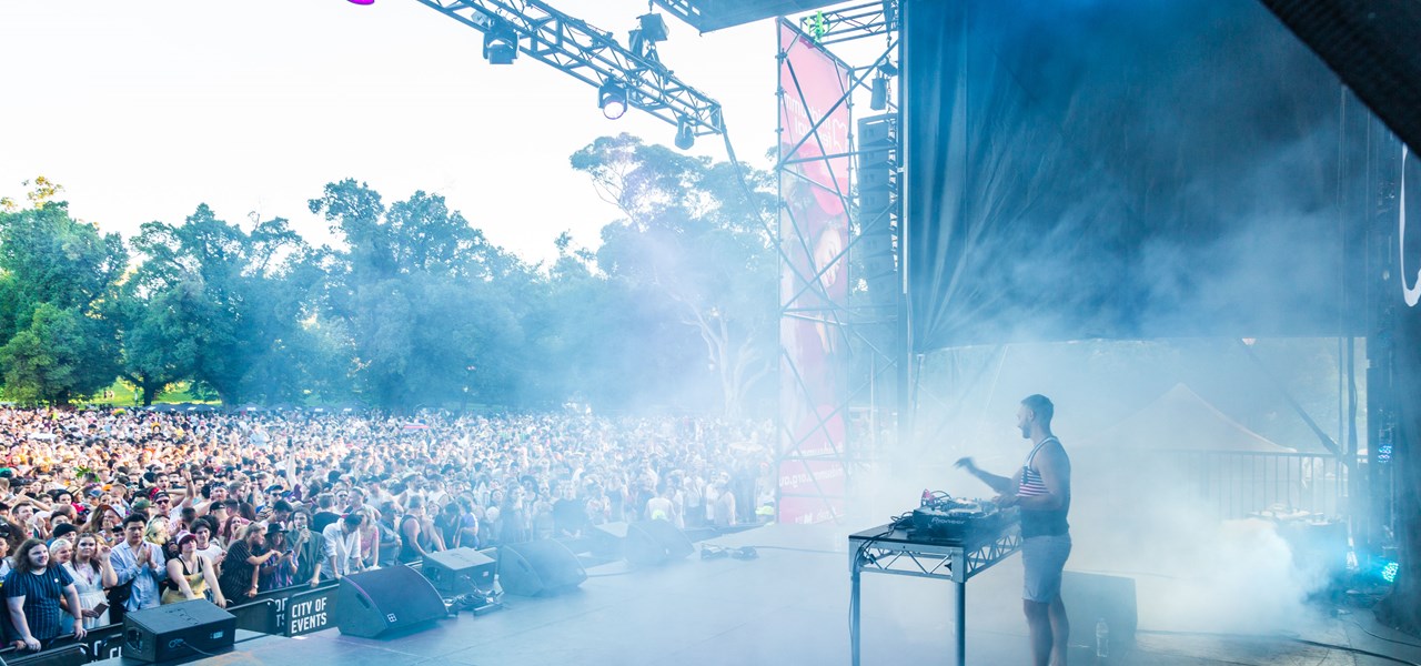 A DJ on a large stage before a large crowd at Midsumma Carnival 2019; lots of smoke present