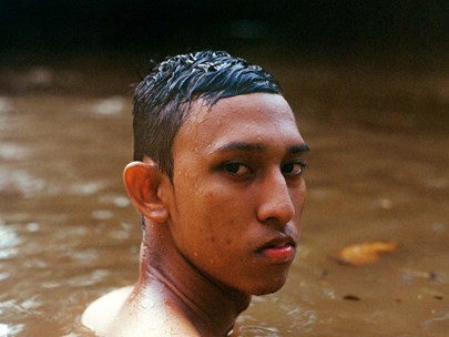 Image of a person in a river. Their body is in profile, but their head is turned so they can gaze accusingly at the camera.