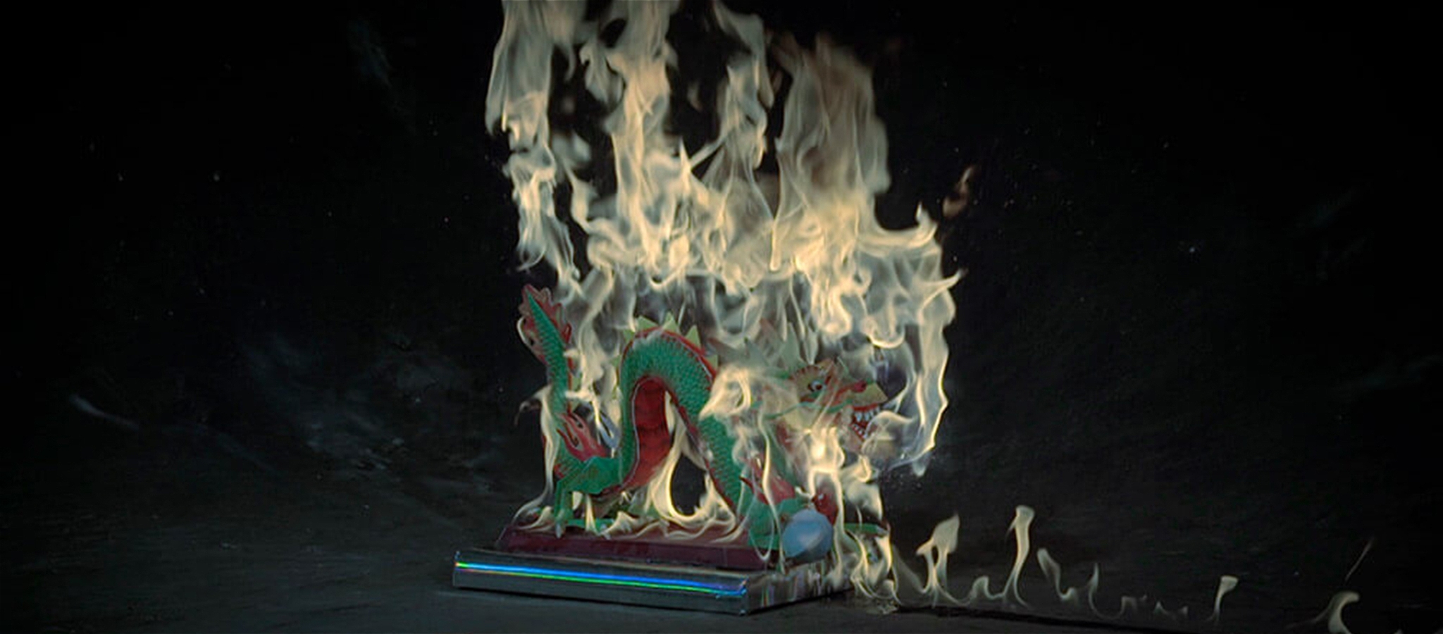 A paper dragon effigy is on fire set on a darkened background