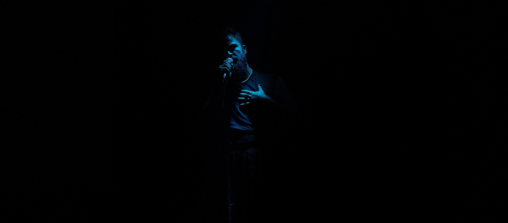 Image of a performer lit in blue light against a black background holding a microphone