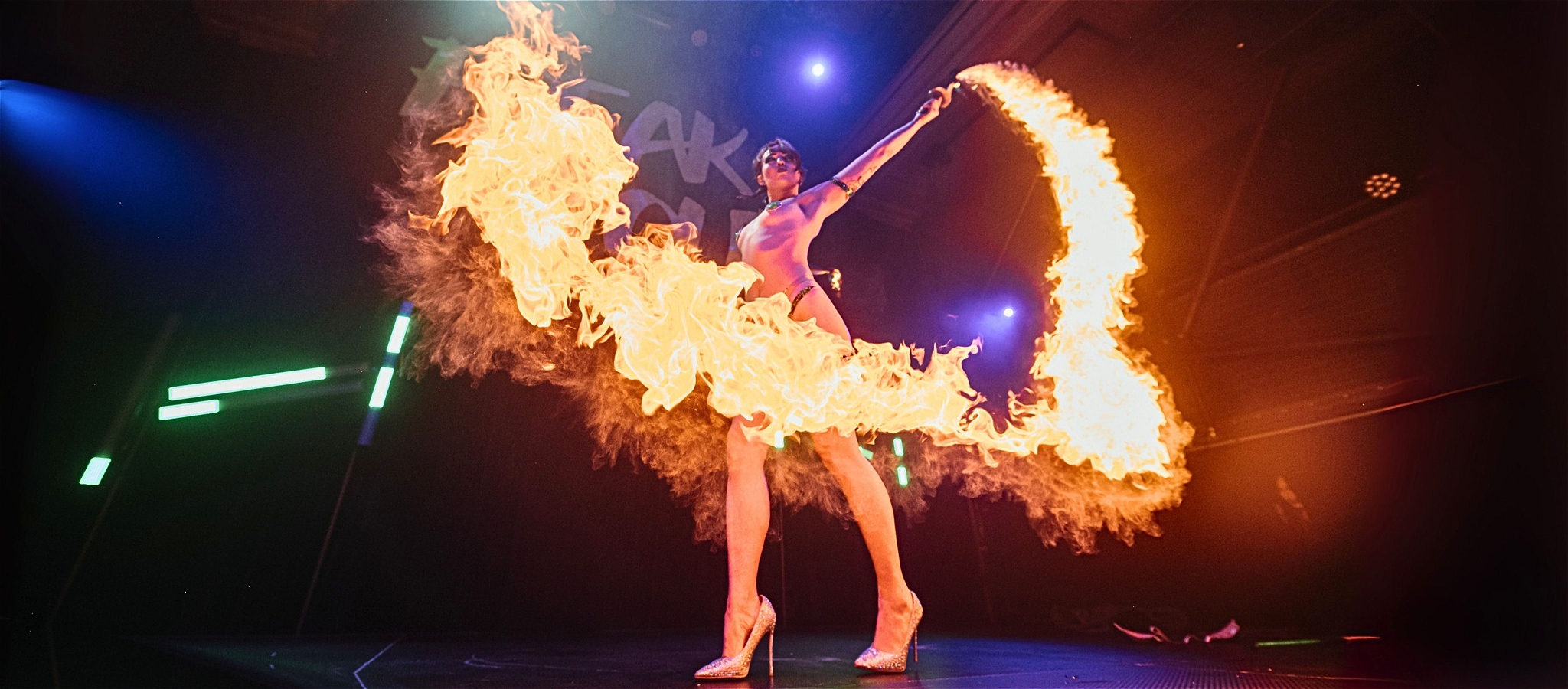 A performer spins a large ring of fire on stage under dramatic lighting.