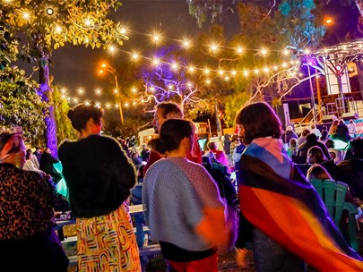 An outdoor event with fairy lights, music and lots of people chilling with friends.