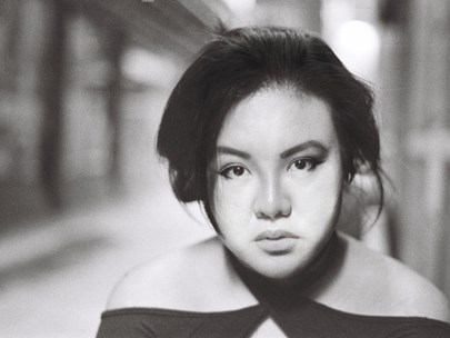 A black-and-white photograph of Angelita looking into the camera with a neutral expression, their dark hair swept back.