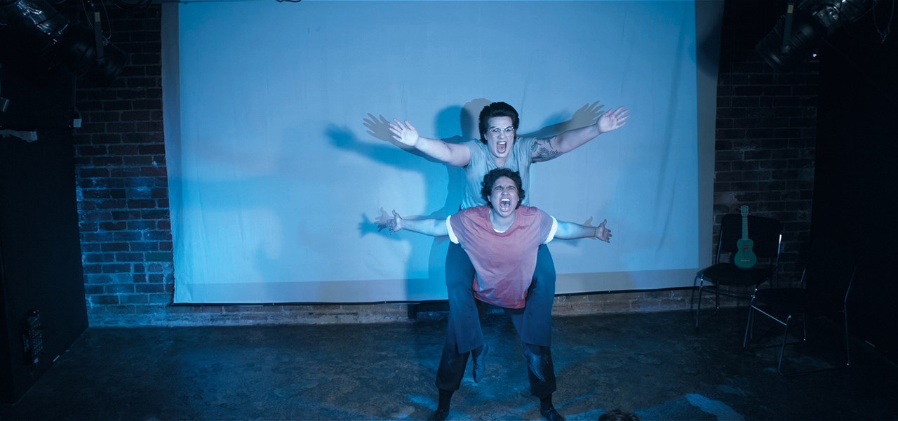 Dylan (Lou Sebial) is flyer and Solar (Neptune Henriksen) base in a piggyback lift. Arms stretched towards audience, and mouths open in a scream.