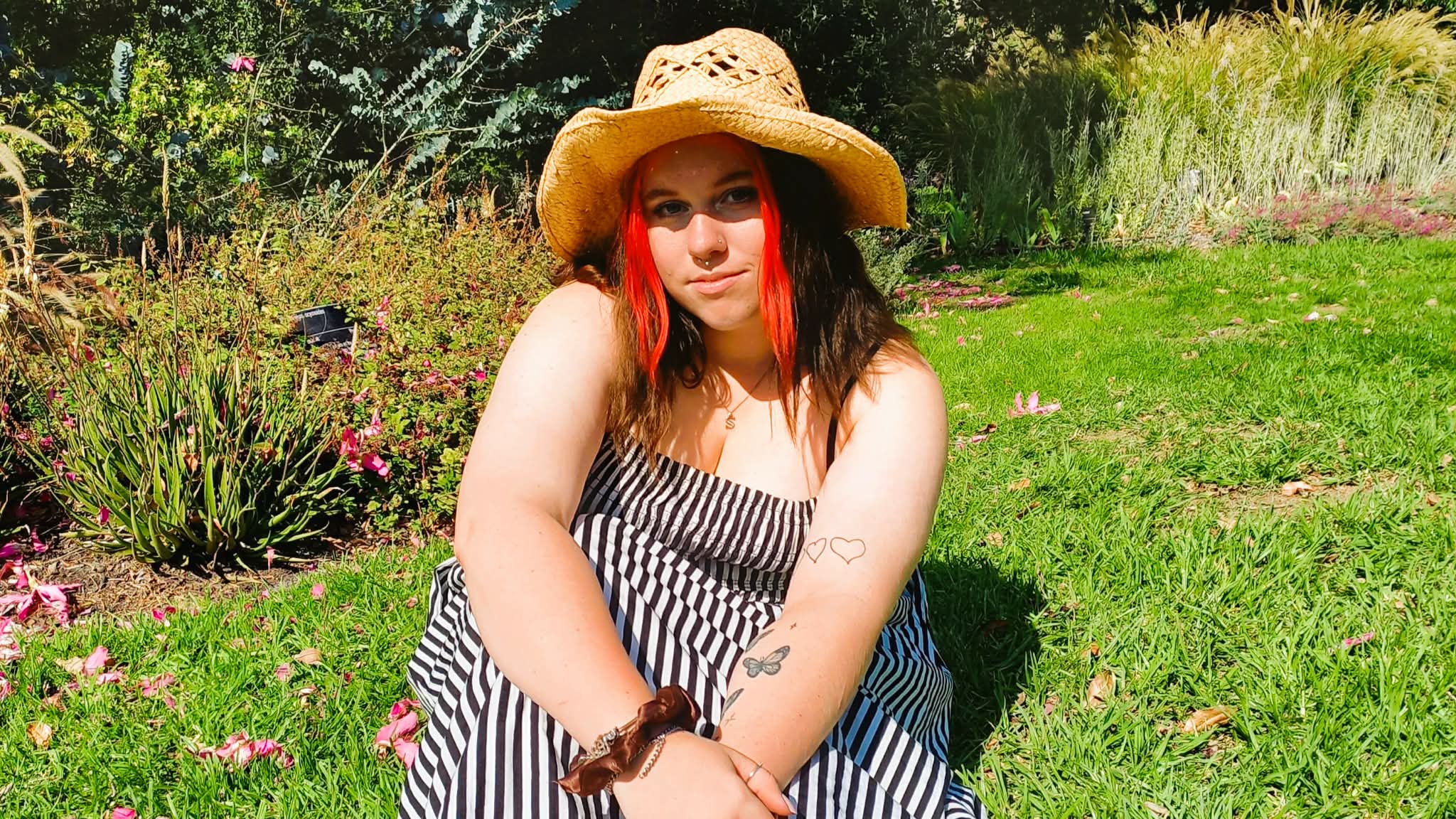 Sage Marie in a summery dress sitting on a lawn in an expansive garden