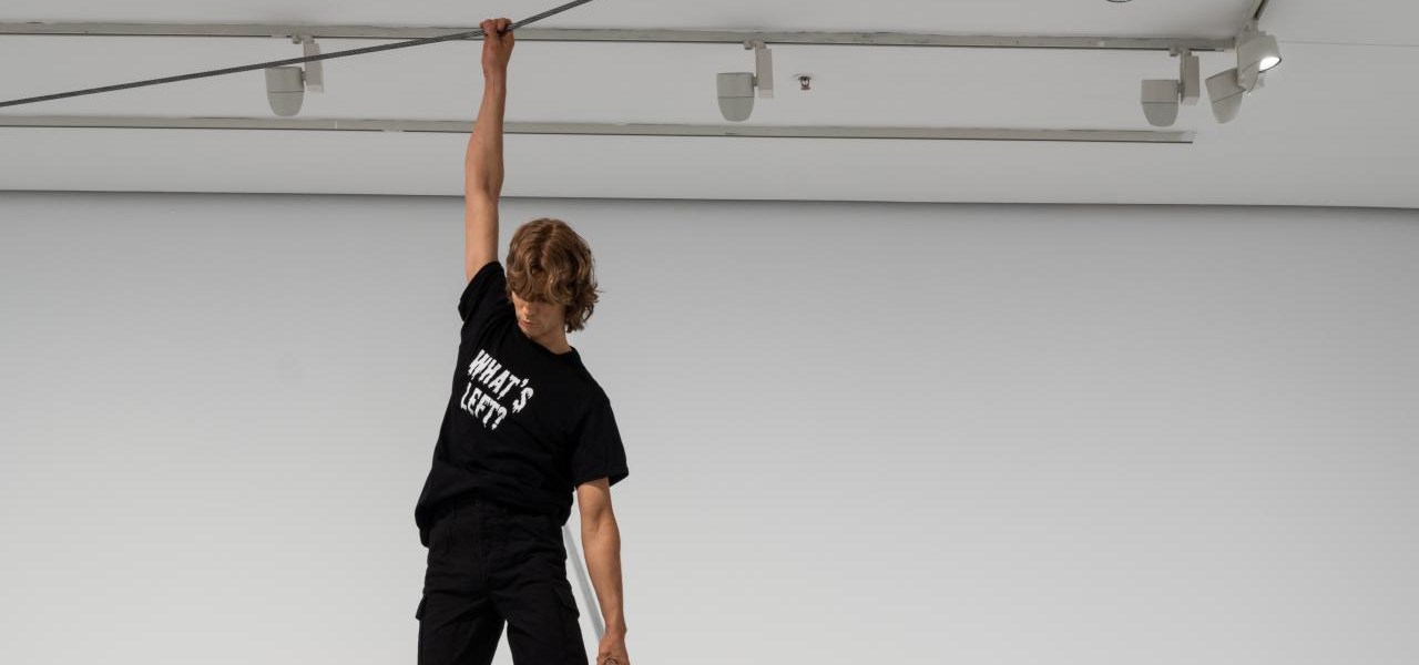 Young acrobat dressed in black gear hanging from a rope near the ceiling