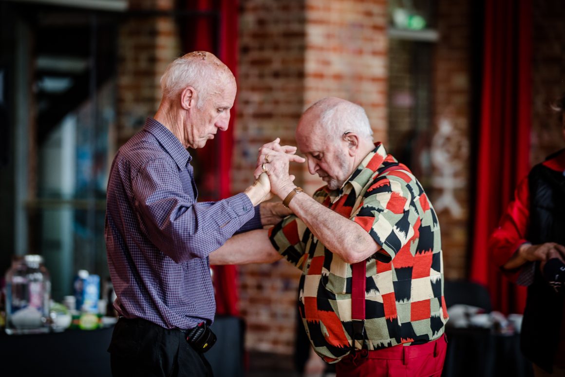 Two old men dancing; one seems to be teaching the other