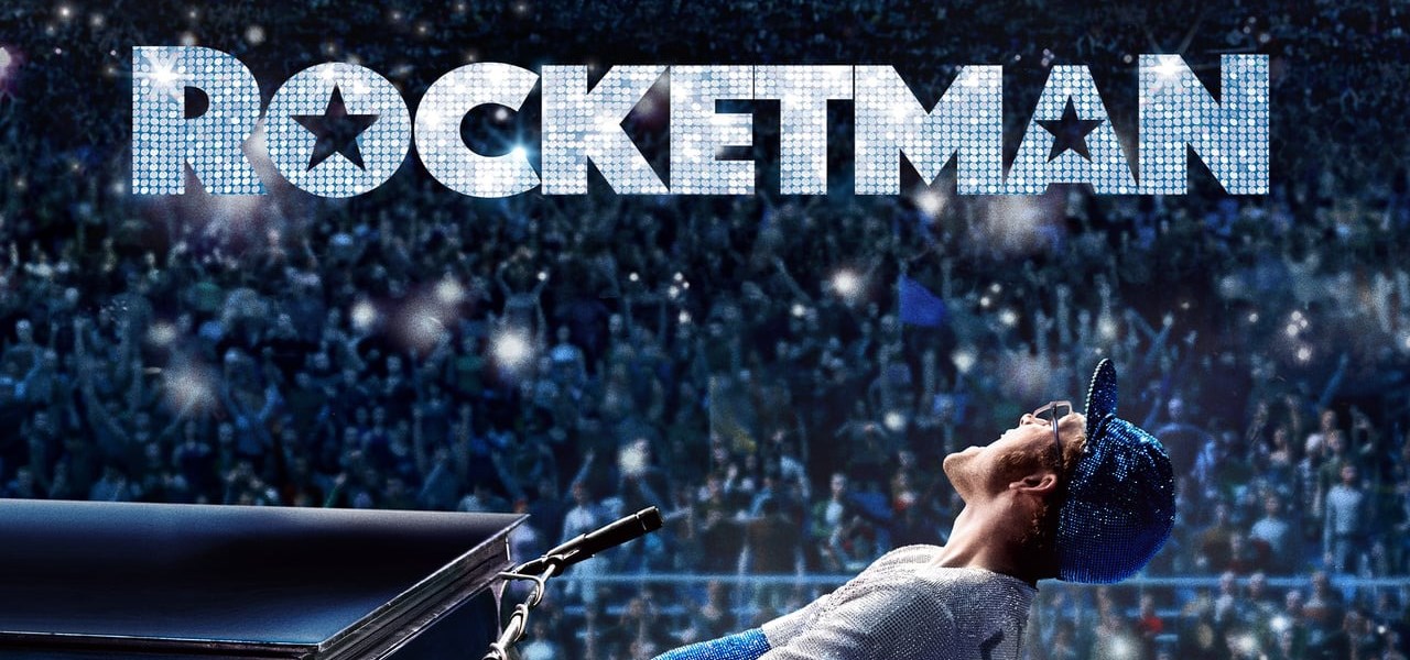 Rocketman sitting at a piano singing energetically with a large stadium crowd behind