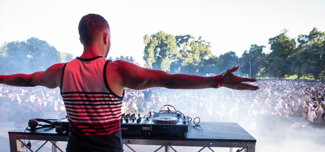DJ standing with arms outstretched facing a large outdoor crowd