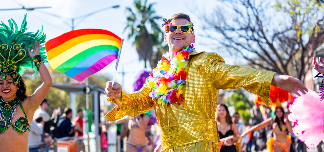 Person dressed in gold with a rainbow garland marching happily at Midsumma Pride March