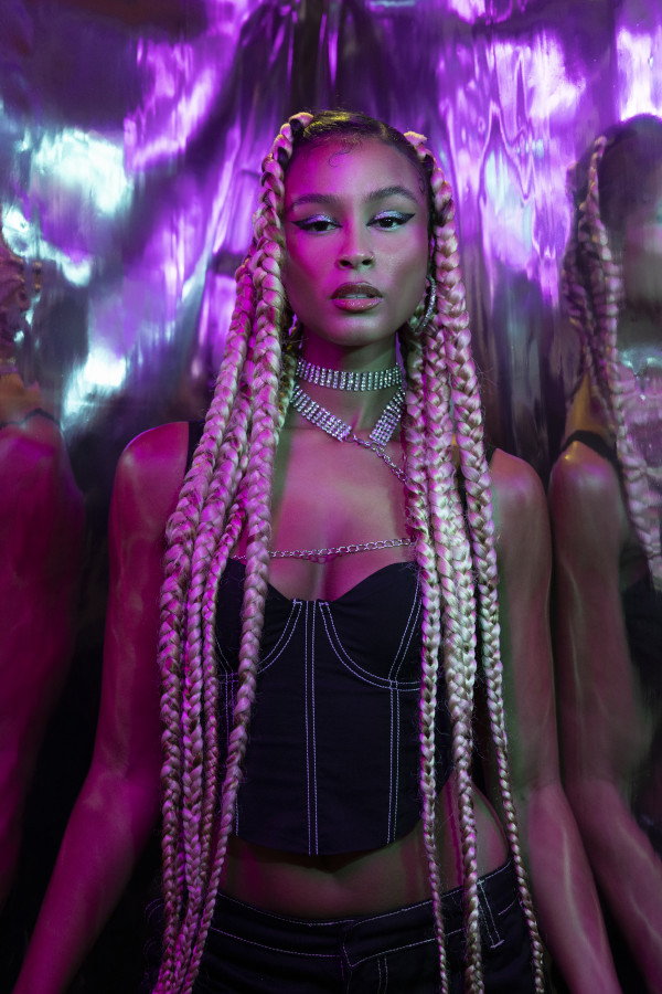 Thandi wearing a skimpy black outfit with braided hair in front of a reflective background