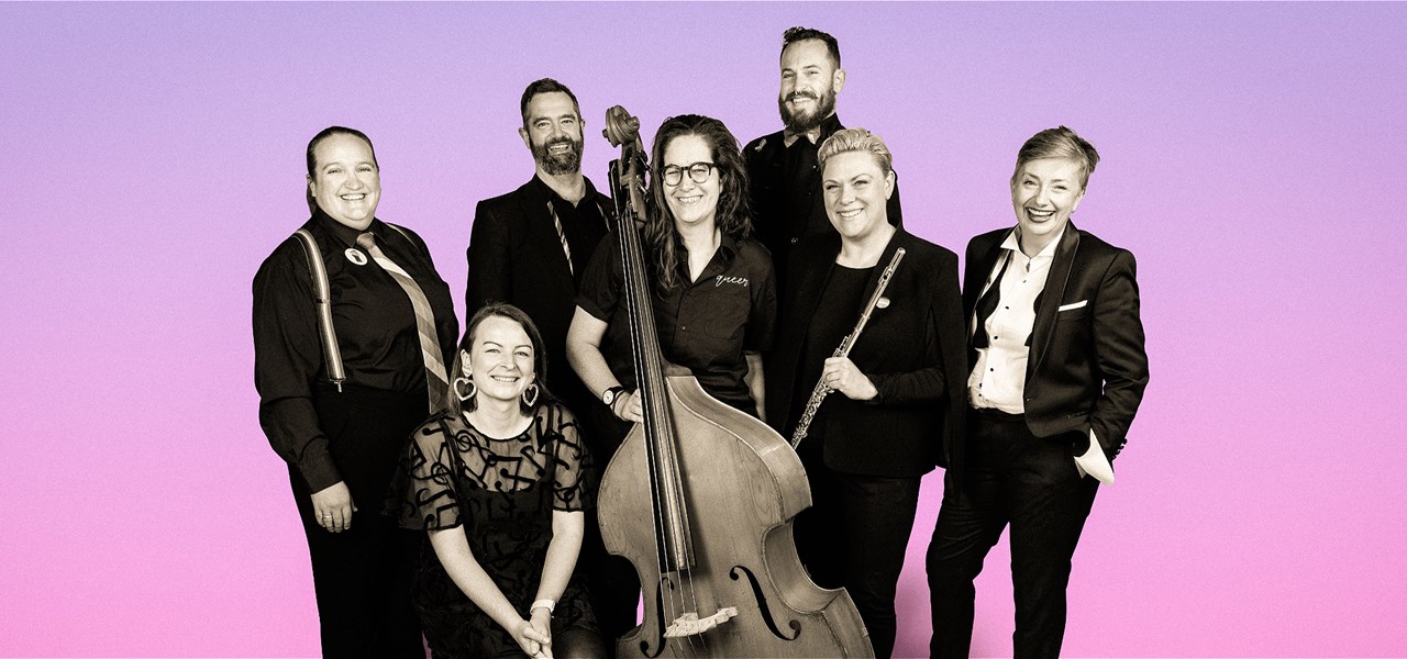 7 musicians together smiling at the camera, the photo is black and white with a purple background. A bass and a flute are held in the centre.