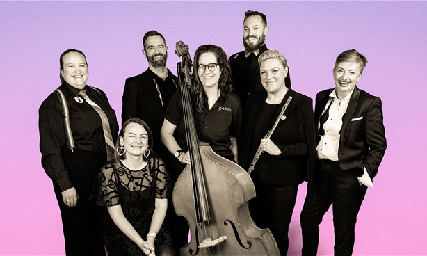 7 musicians together smiling at the camera, the photo is black and white with a purple background. A bass and a flute are held in the centre.