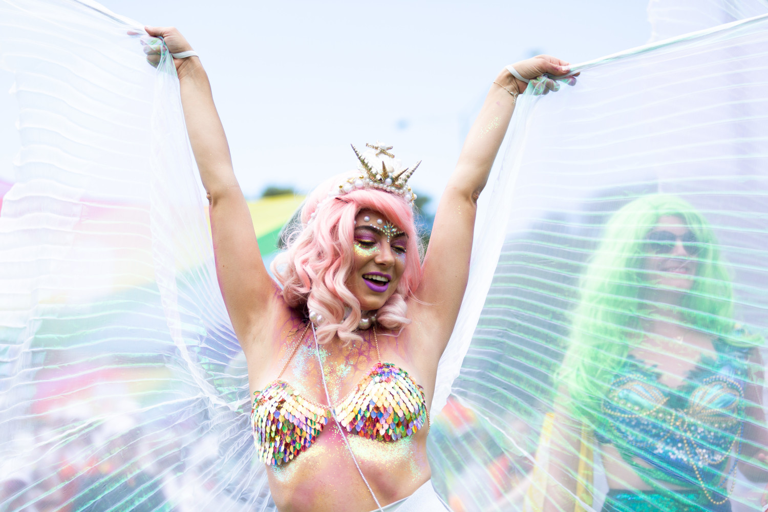 Person in a pink wig, wearing a crown, arms in air looking very happy - gossamer angel wings behind them