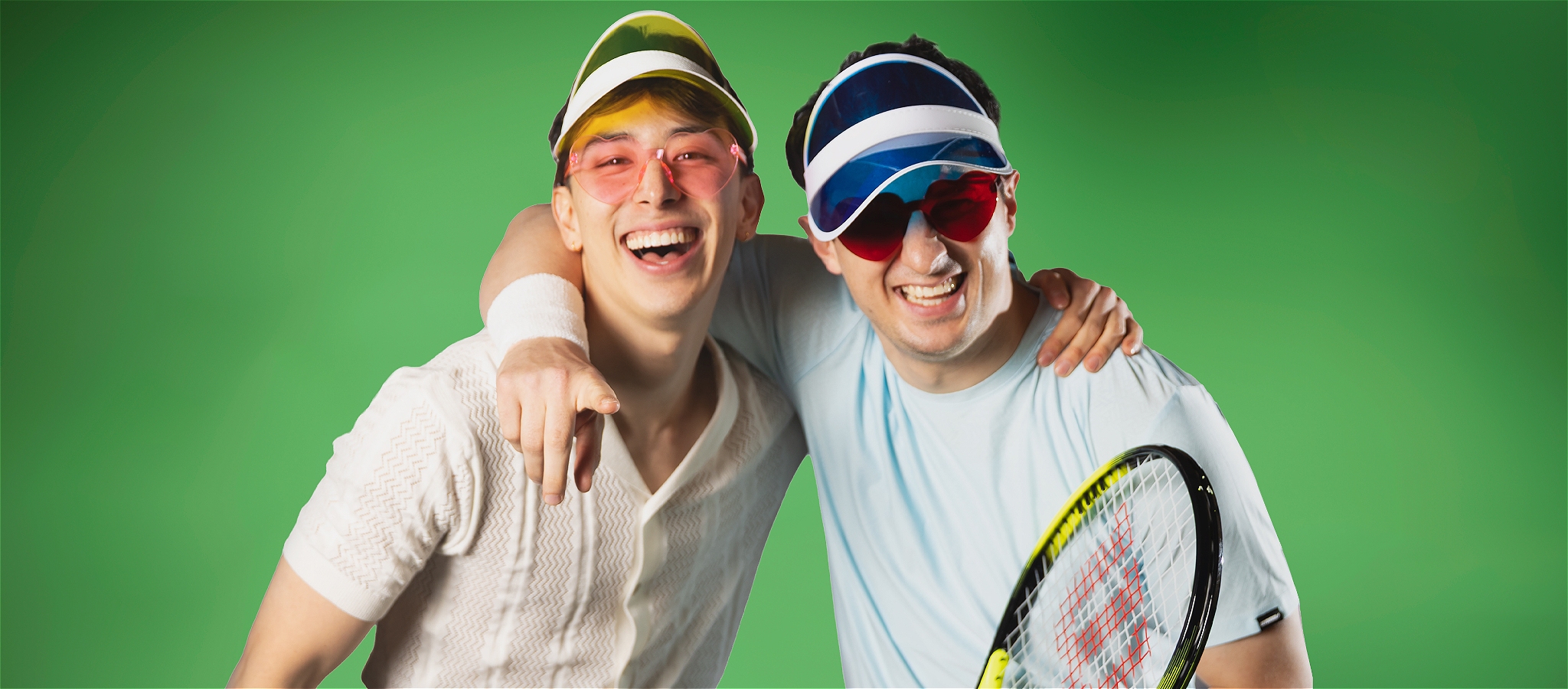 Two elegantly dressed male-identifying people with a tennis racquet in the foreground