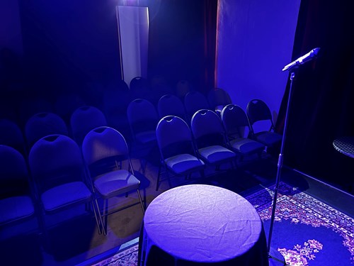 A small room with three rows of chairs and a small stage.