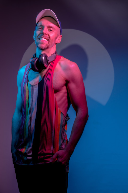 Joelby wearing a singlet and cap with headphones around their neck, smiling