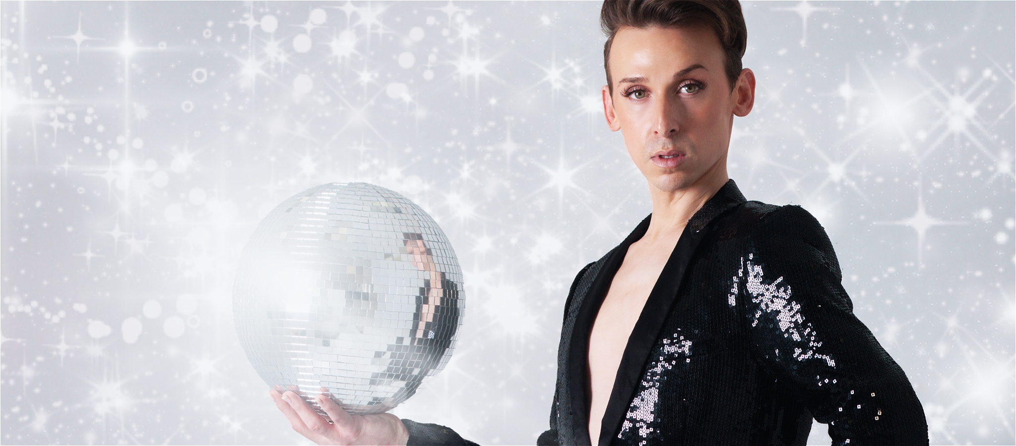 Justin Clausen shines in sequins, striking a bold pose with disco balls amid sparkling light.